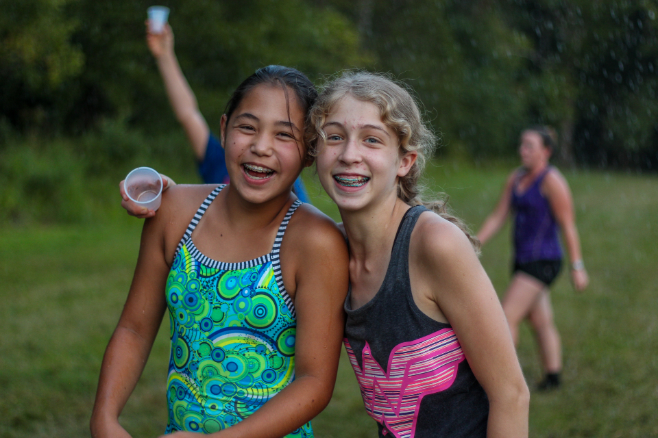 Two junior girl campers forget all about their phones as they take part in a massive water fight on our soccer field at Camp Friendship.