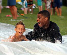 A junior boy camper speeds down our slip n' slide with his cabin counselor.