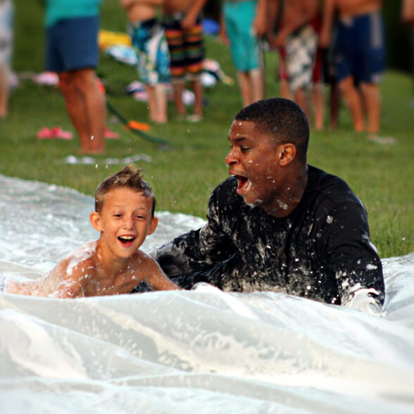 A junior boy camper speeds down our slip n' slide with his cabin counselor.