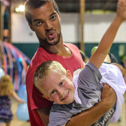 A junior counselor helps his camper "fly" at the camp dance. 