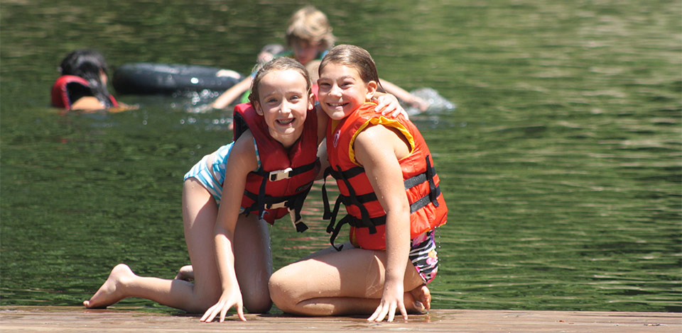 Two junior campers in life jackets by the lake