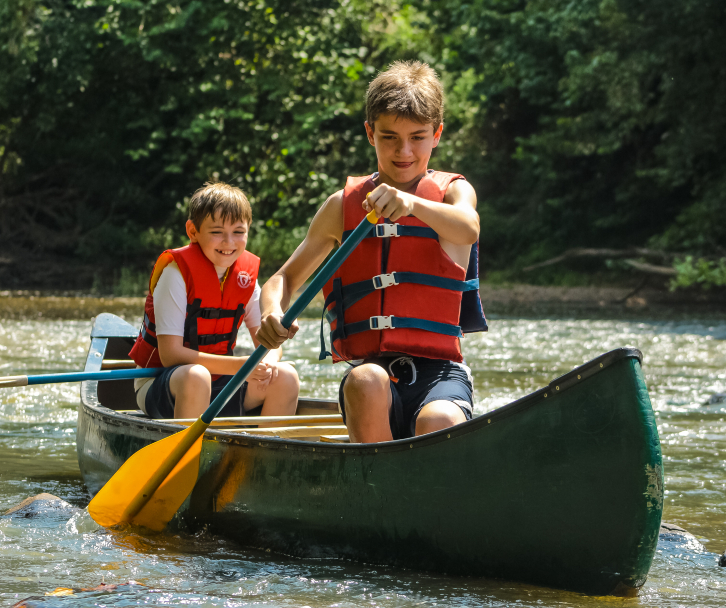 Two young campers paddle their canoe along Friendship Lake at a coed sleep-away summer camp