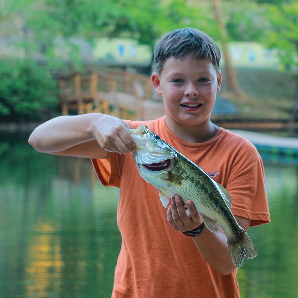 Senior Village camper holding a fish he caught at summer camp