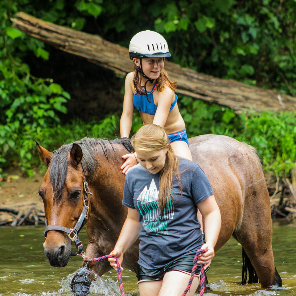 Camper and staff enjoy cooling off with a river ride on horseback at the Camp Friendship overnight camp in Virginia