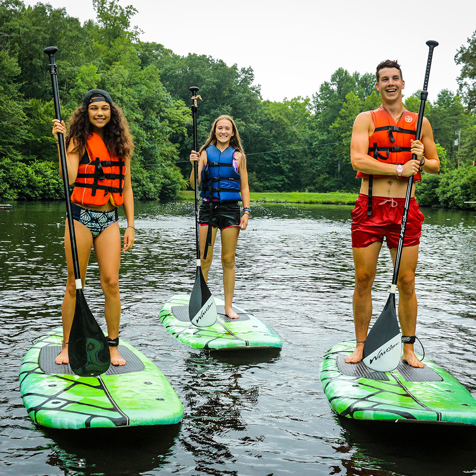 Two campers and a counselor paddle-boarding at Friendship Lake summer camp