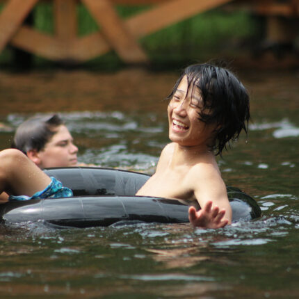A senior village camper laughs as he sits in an inner tube floating through Friendship Lake.