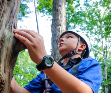 A teen camper challenges himself by climbing the pamper pole, one of our high ropes elements.