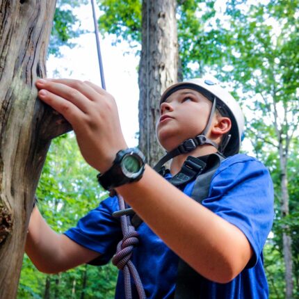 Young boy camper climbs an element at the High Ropes activity at overnight camp in Virginia