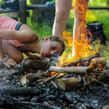 Girl Camper blows on campfire to keep it burning