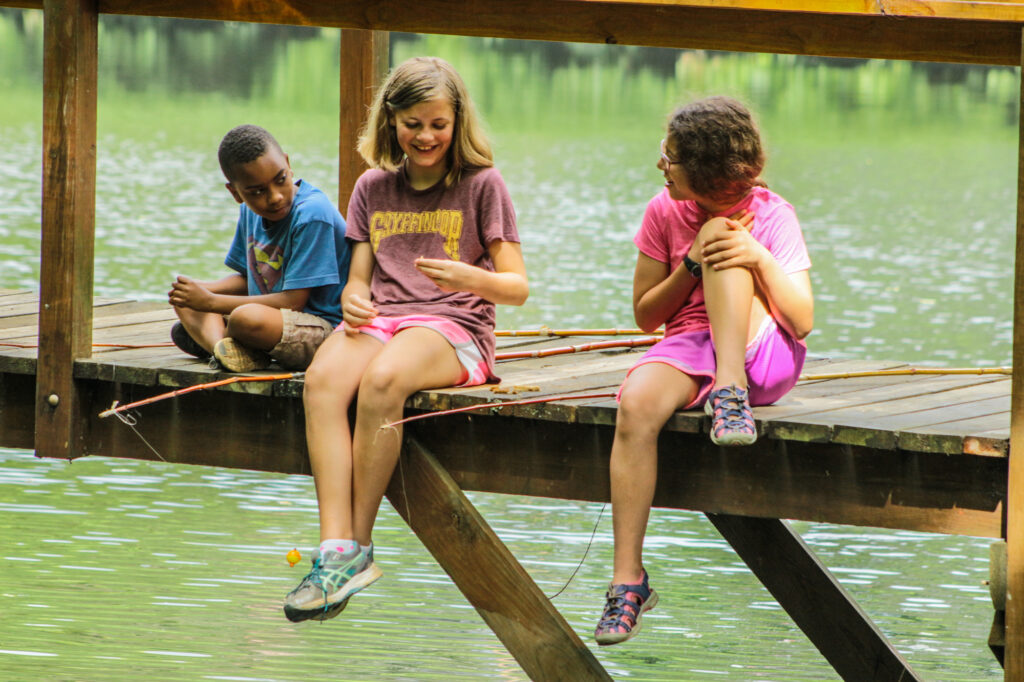 Junior campers dressed in clothes that can get wet are more than prepared for this fishing session by friendship lake.