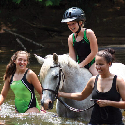 A camper and two counselors enjoy a river ride on horseback at Camp Friendship overnight Equestrian Camp
