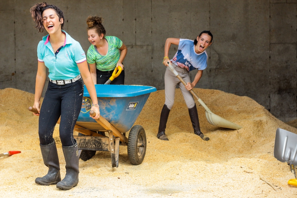 Three girls gather bedding for their horses' stalls at an overnight Equestrian camp as part of their barn chores. 