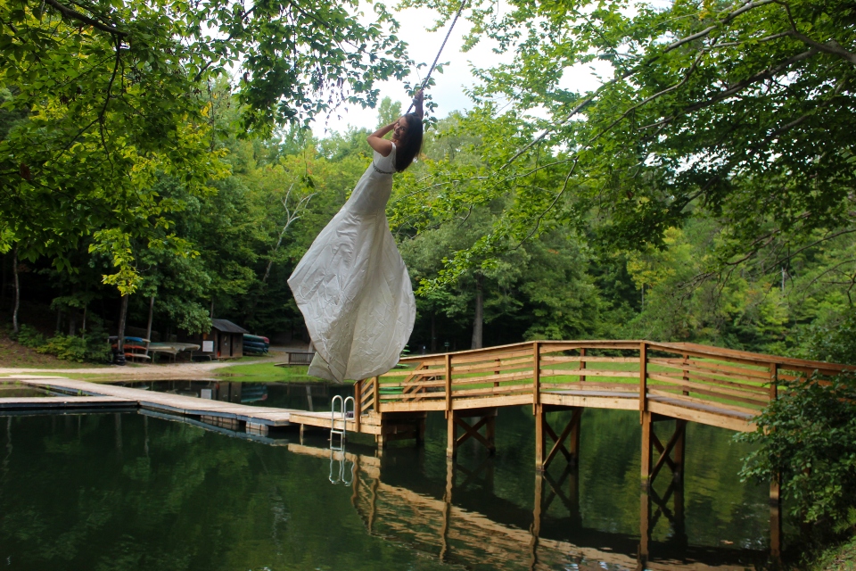 Bride in wedding gown swings over the water of Friendship Lake on rope swing