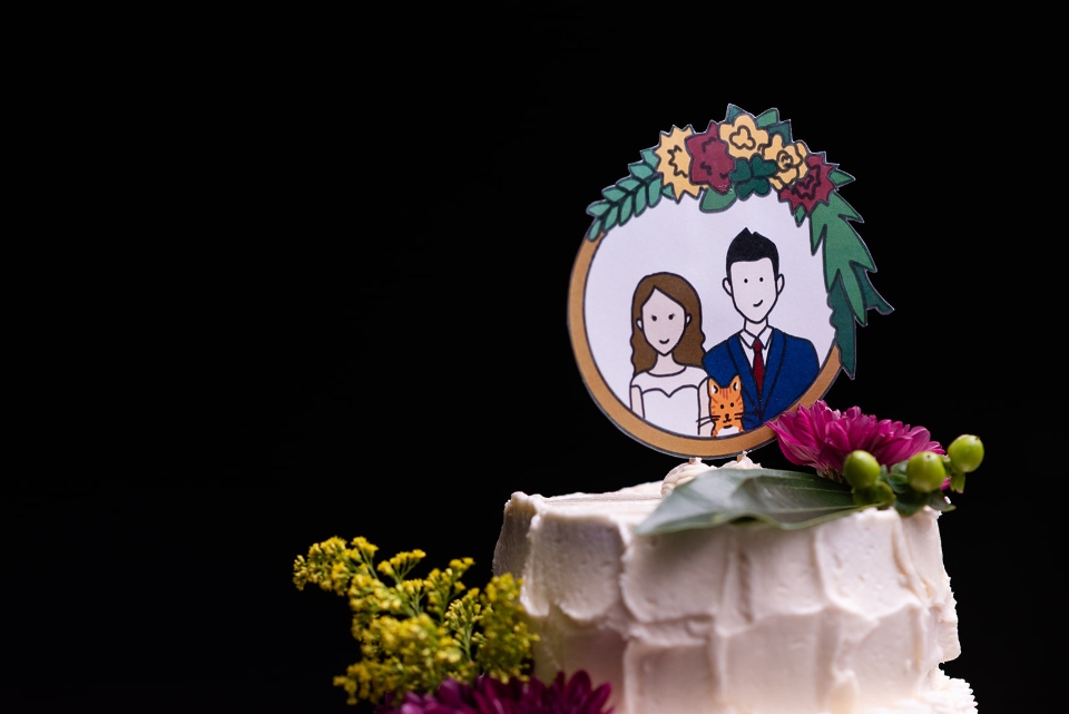 A delicious white wedding cake topped by a portrait of the bride and groom from one of our weddings is shown.