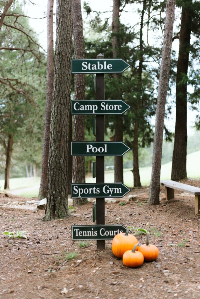 Directional sign with the following words "Stable", "Camp Store", "Pool", "Sports Gym", and "Tennis Courts"