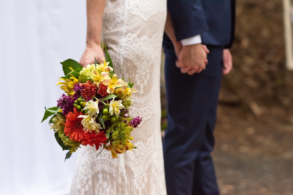 The holding hands of a bride and groom are shown as the bride holds her bouquet after her wedding.