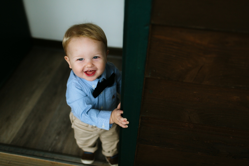 A young child in dress clothes and a bow tie smiles with joy as he gets ready for the wedding.
