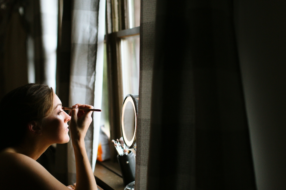A bride applies her make up as she gets ready for her summer camp wedding.