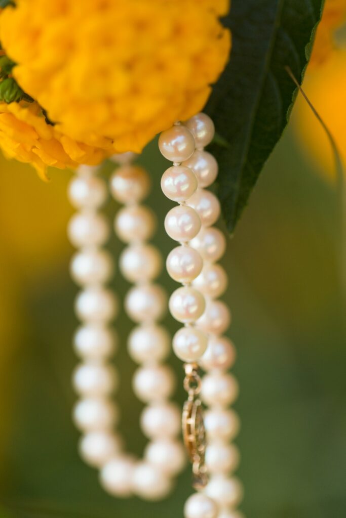 A close up of a bride's pearls hanging from the flowers of her bouquet.