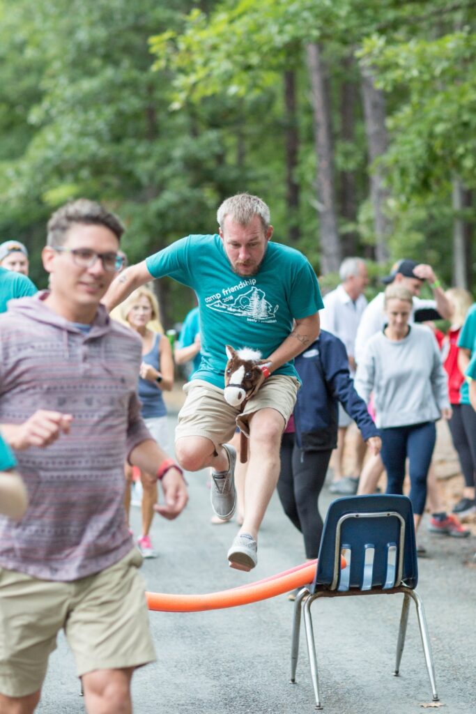 Man with hobby horse hurdling over barrier as part of a wedding activity ay Camp Friendship