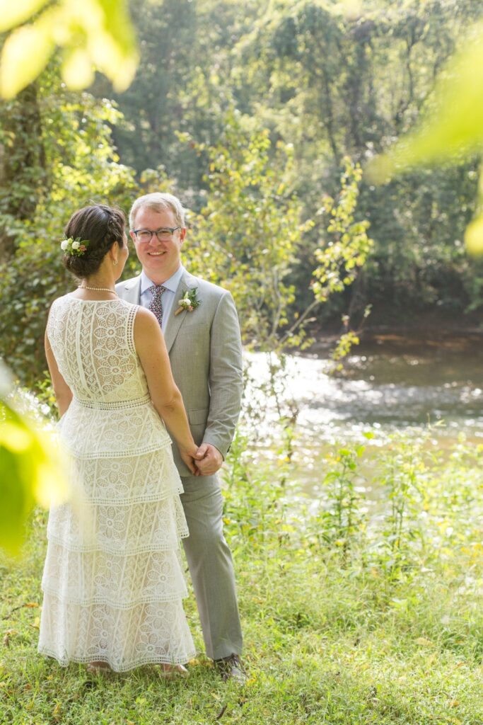 Bride and Groom holding hands in greenery next to Rivanna river at Virginia summer camp wedding