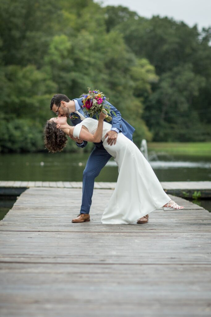 Groom dips bride and kisses her on the dock on the lake at Camp Friendship