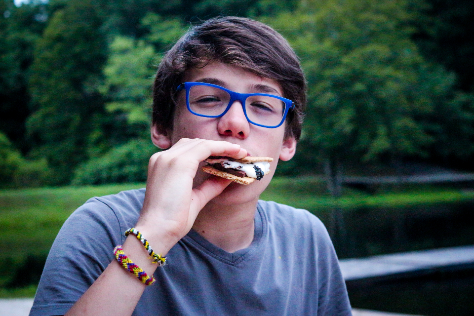 A senior camper enjoys the first s'more of summer at a cookout by friendship lake.