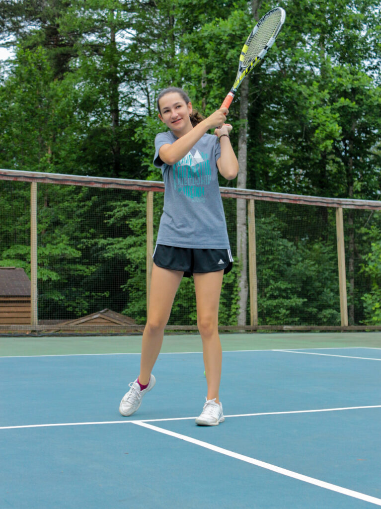 Teen girl swings her tennis racket at Camp Friendship summer tennis program