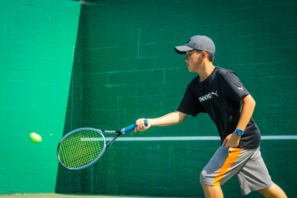 Boy hitting tennis ball with racket at tennis summer program