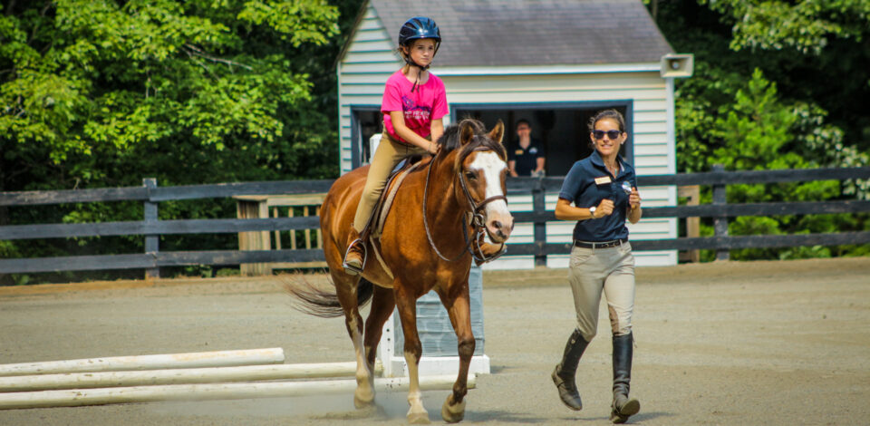 A director helps one of our overnight equestrian campers practice for our horse show.