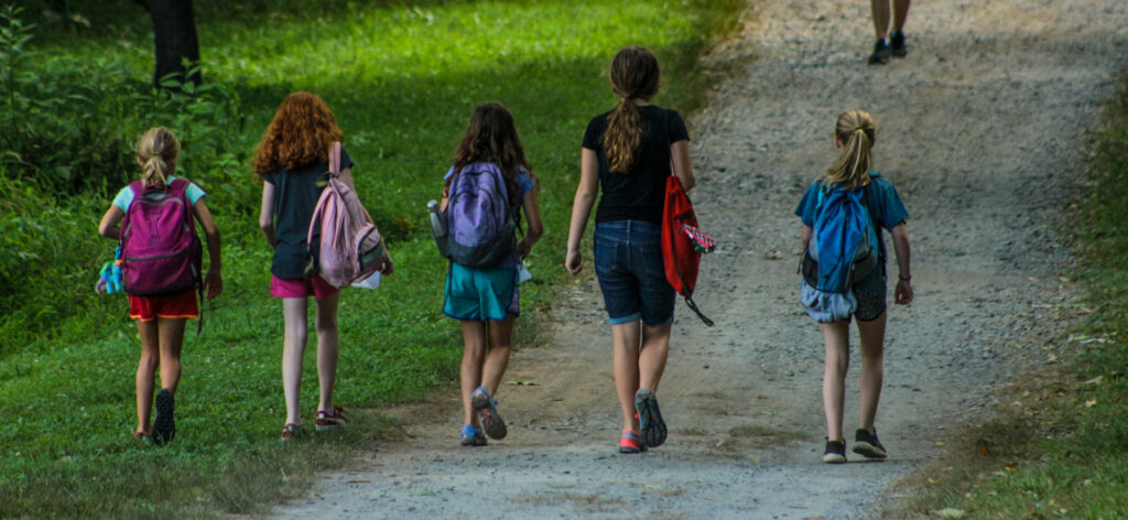 Five girls with backpacks walk along path at Camp Friendship