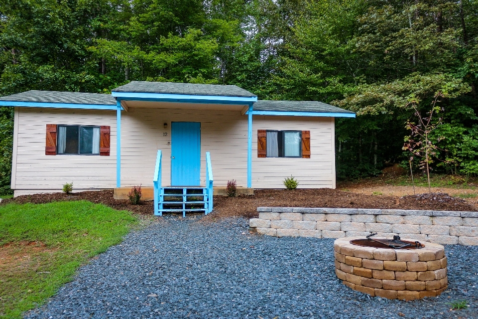 White cabin with blue door and trim at end of gravel path with fire pit