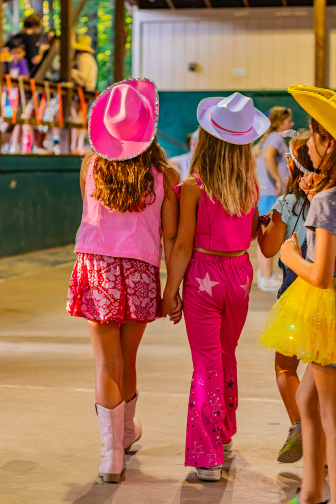 2 girls in pink cowboy outfits holding hands with their back to the camera