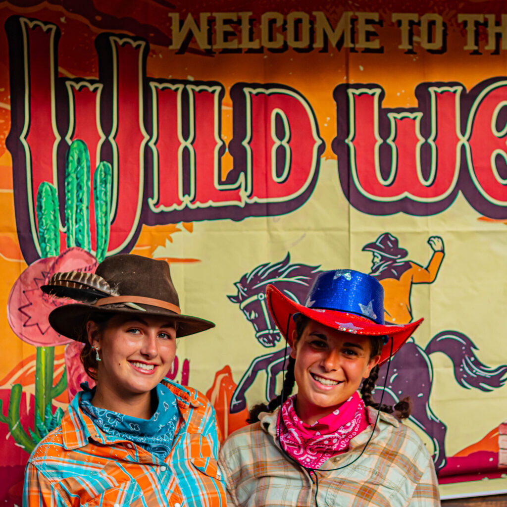 2 girls wearing cowboy costumes in front of a decorative background that says "Welcome to the Wild West"