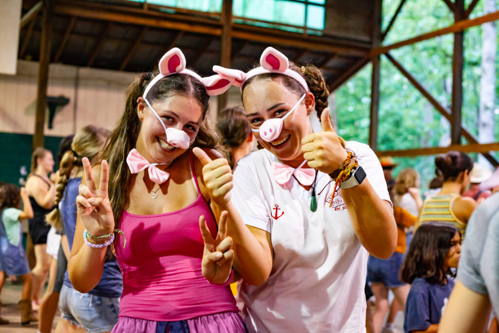 Two girls wearing pig costumes smiling and giving a thumbs up to the camera