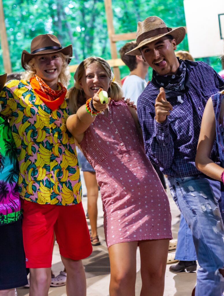 3 people in wild west costumes smiling and 2 of them pointing at the camera