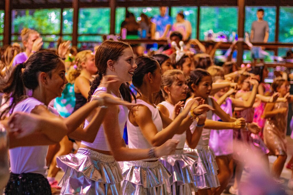 Group of girls smiling and dancing facing to the right with their arms outstretched
