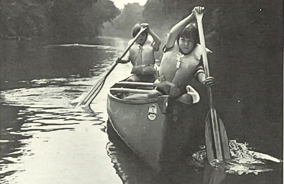 A black and white photo of two children paddling a canoe